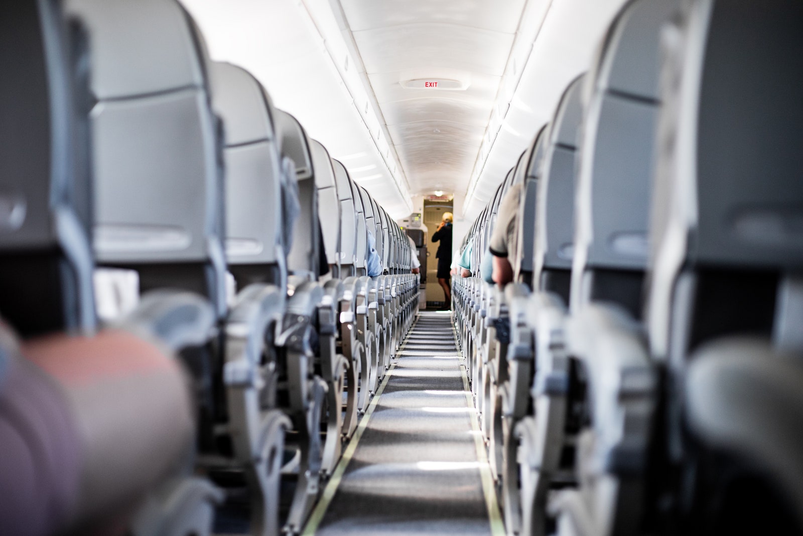 Photo of illuminated commercial aircraft cabin with rows of gray seats down aisle with aircraft crew members standing at...